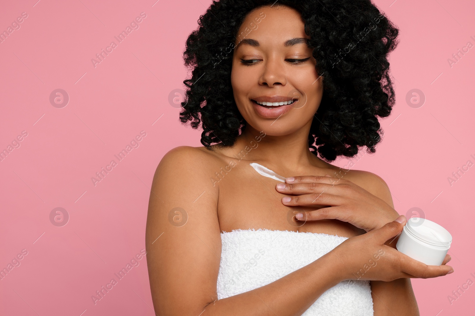 Photo of Young woman applying cream onto body on pink background. Space for text