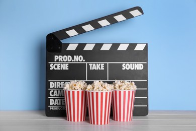 Delicious popcorn and clapperboard on light wooden table
