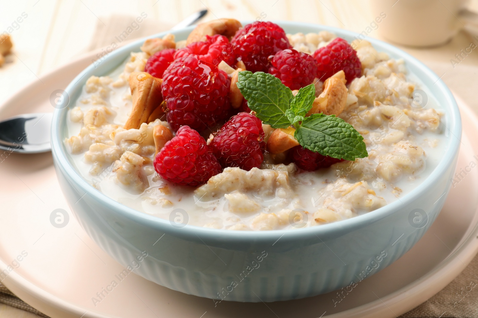 Photo of Bowl with tasty oatmeal porridge with nuts and raspberries on table, closeup. Healthy meal