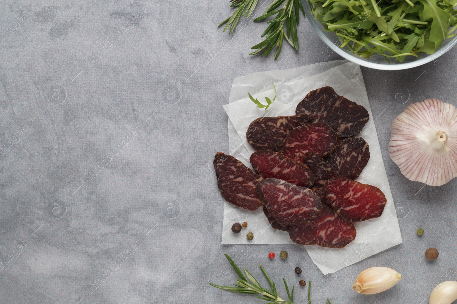 Photo of Slices of delicious beef jerky and spices on grey marble table, flat lay. Space for text