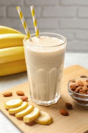 Photo of Banana smoothie in glass and nuts on table against white brick wall