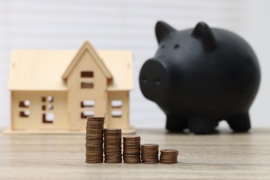 House model, piggy bank and stacked coins on wooden table, selective focus