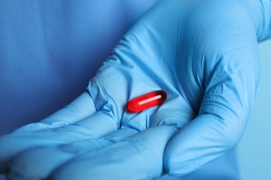 Photo of Doctor in medical glove holding pill on turquoise background, closeup