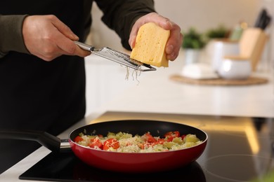 Photo of Cooking process. Man grating cheese into frying pan in kitchen, closeup