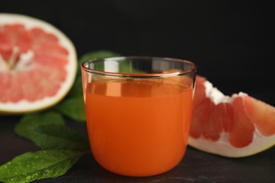 Photo of Glass of pink pomelo juice, fruit and green leaves on black table, closeup