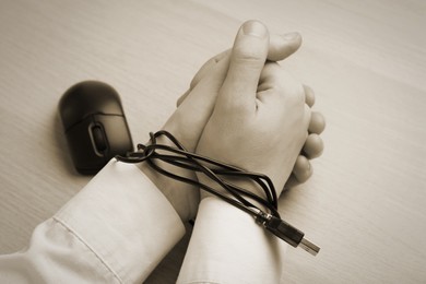 Image of Closeup view of woman with her hands tangled in cable of computer mouse at wooden table, sepia effect. Internet addiction