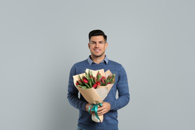 Happy man with red tulip flowers bouquet on light grey background. 8th of March celebration