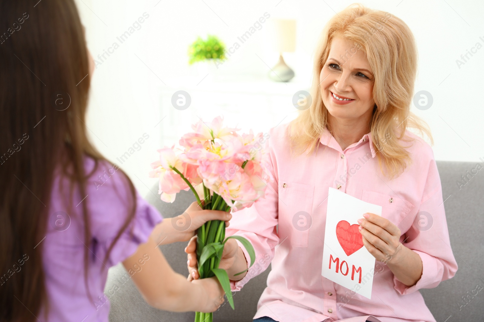 Photo of Little daughter congratulating her mature mom at home. Happy Mother's Day