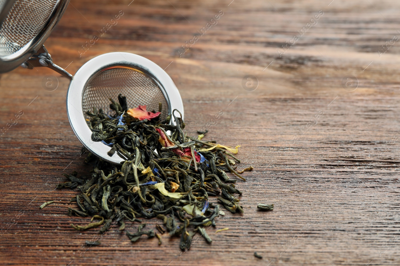 Photo of Snap infuser with dried herbal tea leaves on wooden table, closeup. Space for text