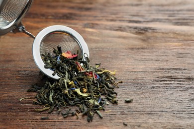 Snap infuser with dried herbal tea leaves on wooden table, closeup. Space for text