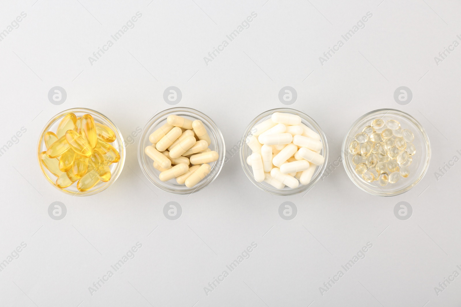 Photo of Different vitamin capsules in glass bowls on light grey background, flat lay