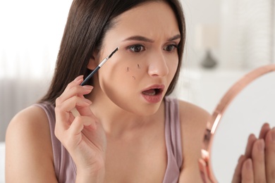 Photo of Beautiful woman with fallen eyelashes and cosmetic brush looking into mirror indoors