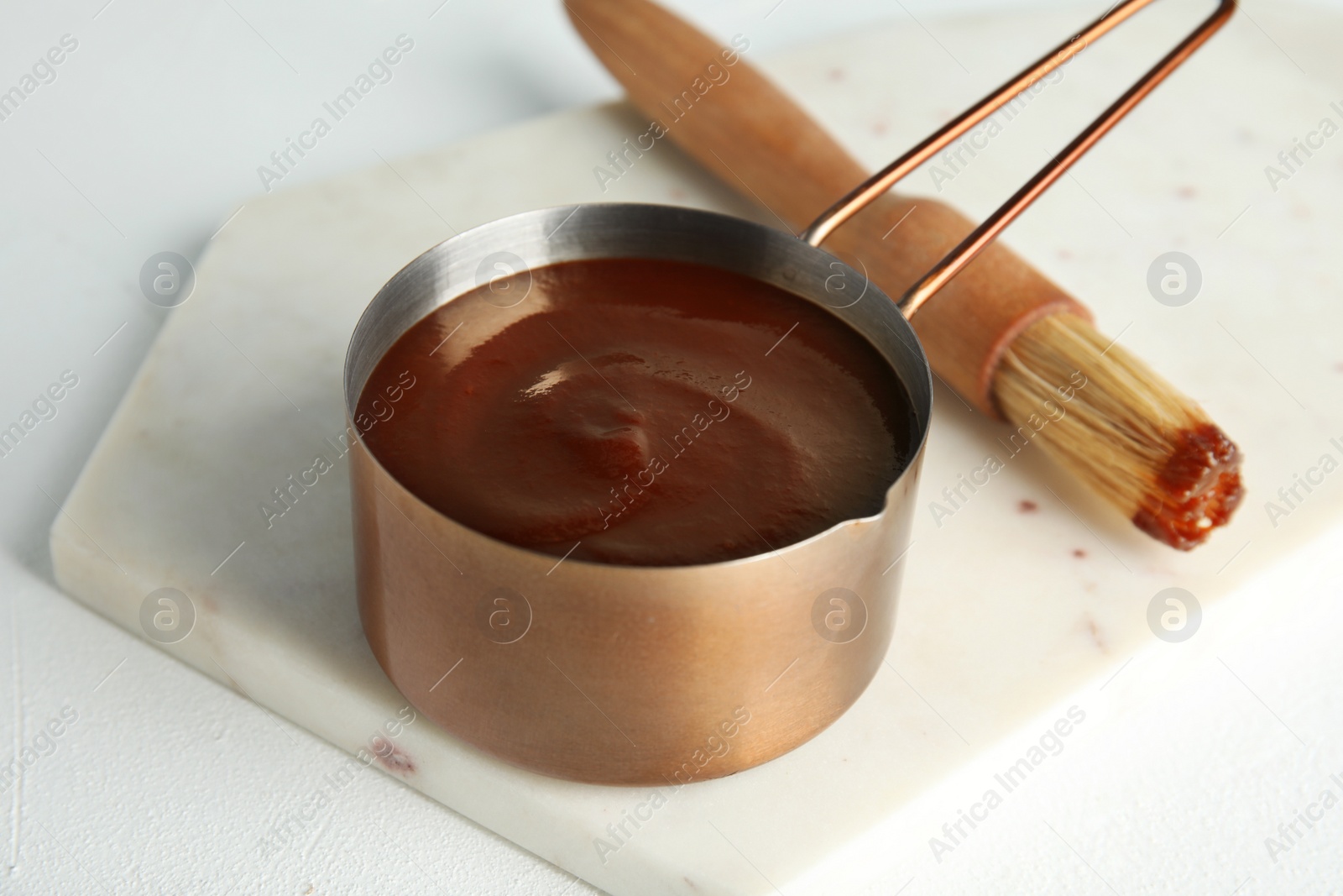 Photo of Cooking pot with barbecue sauce and brush on white table