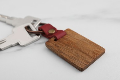 Photo of Keys and wooden keychain with Ukrainian coat of arms on white marble table, closeup
