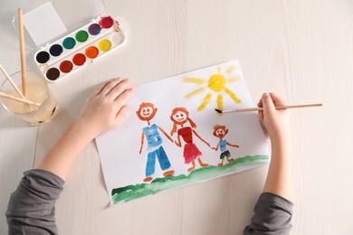 Photo of Little boy drawing picture at wooden table, top view. Child`s art