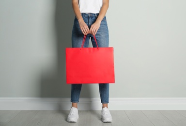 Photo of Woman with paper shopping bag near light grey wall, closeup