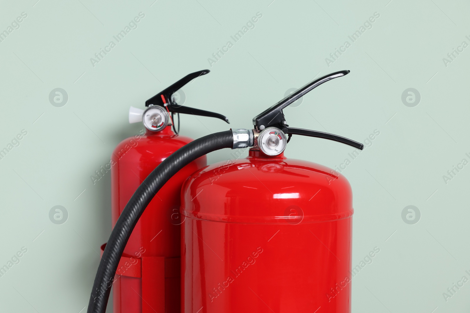 Photo of Red fire extinguishers against light green background, closeup
