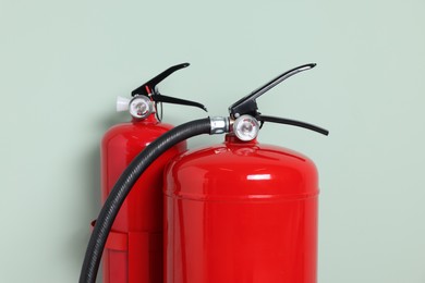 Red fire extinguishers against light green background, closeup