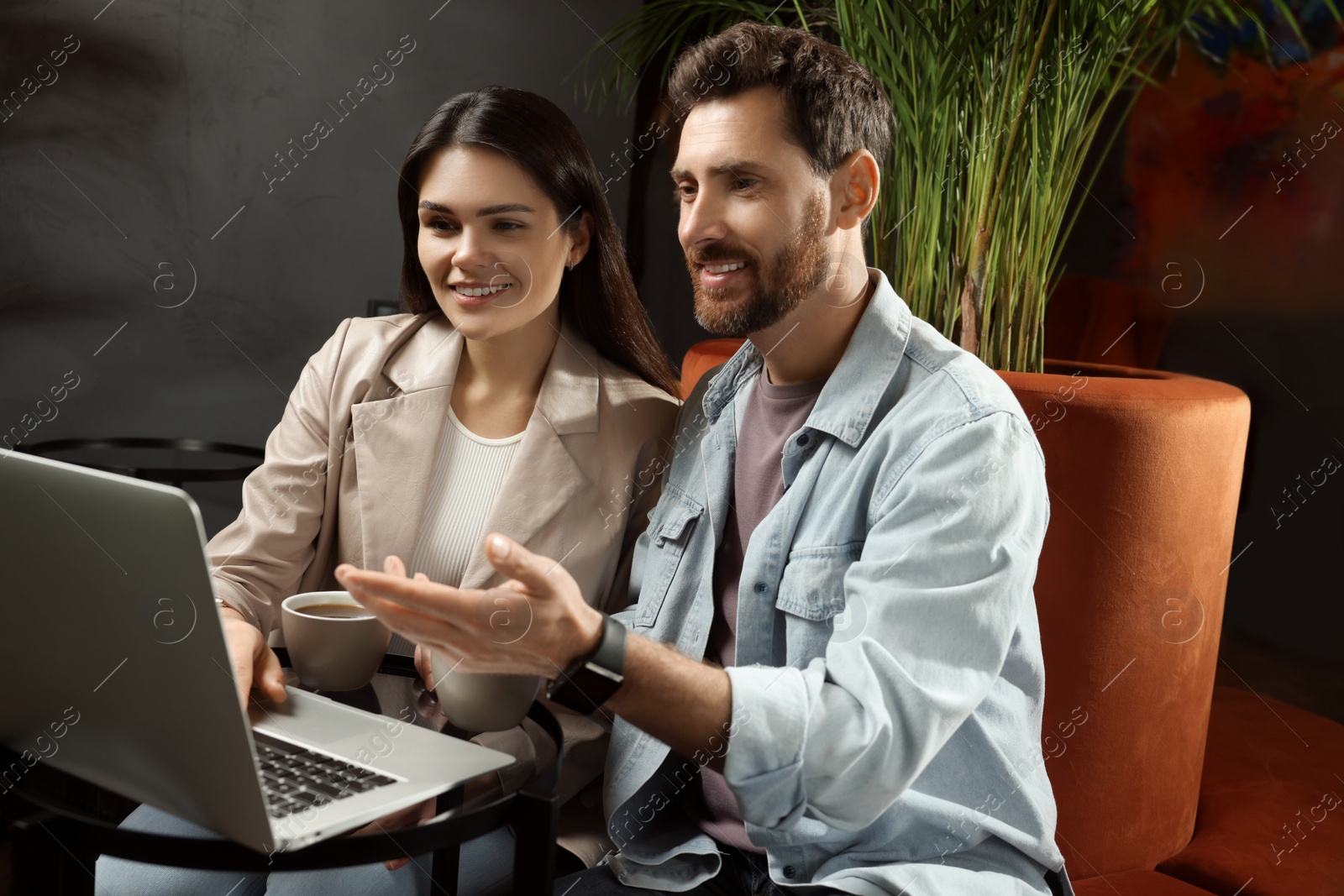 Photo of Couple with coffee and laptop spending time together in cafe