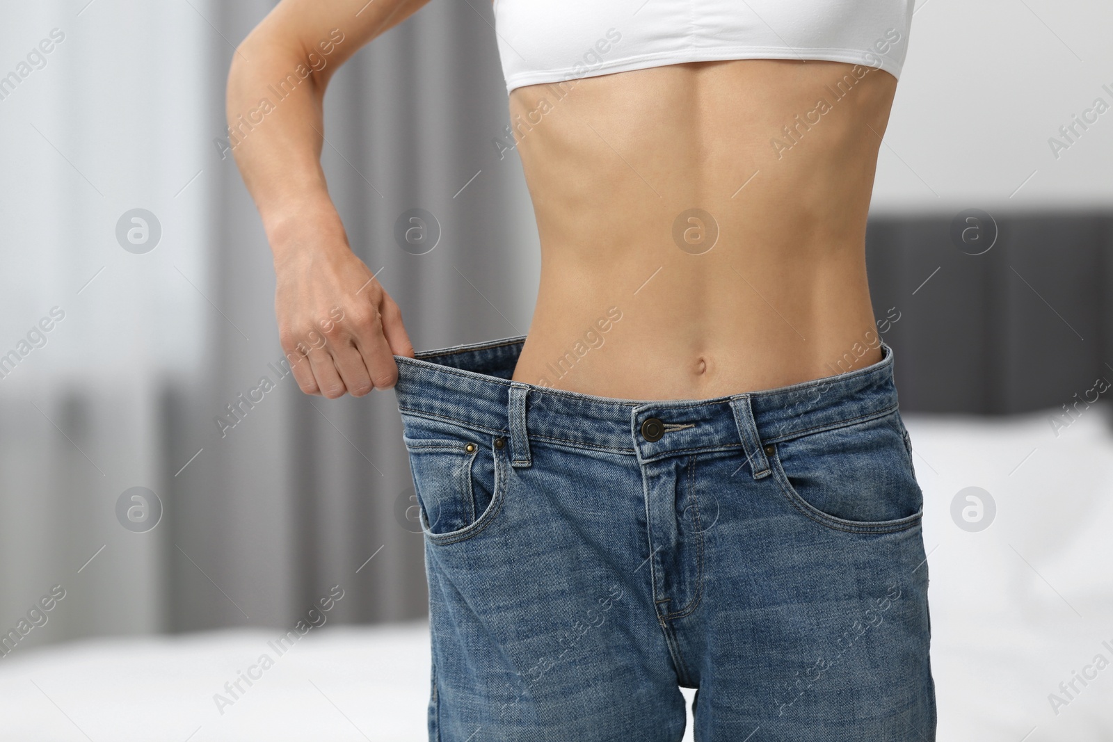 Photo of Slim woman wearing big jeans at home, closeup. Weight loss