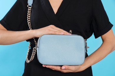 Woman with stylish bag on light blue background, closeup