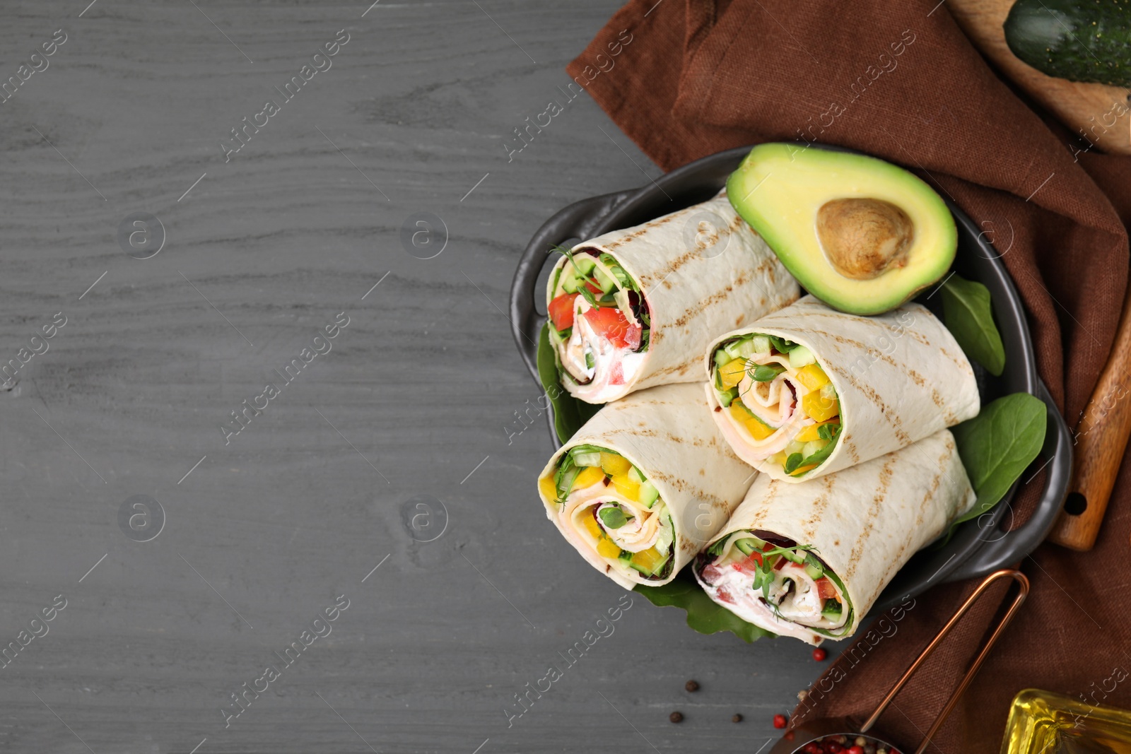 Photo of Delicious sandwich wraps with fresh vegetables and avocado on grey wooden table, flat lay. Space for text