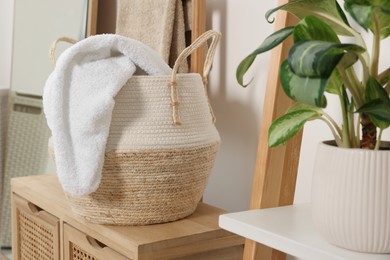 Photo of Wicker basket with white soft towel on wooden stand in bathroom