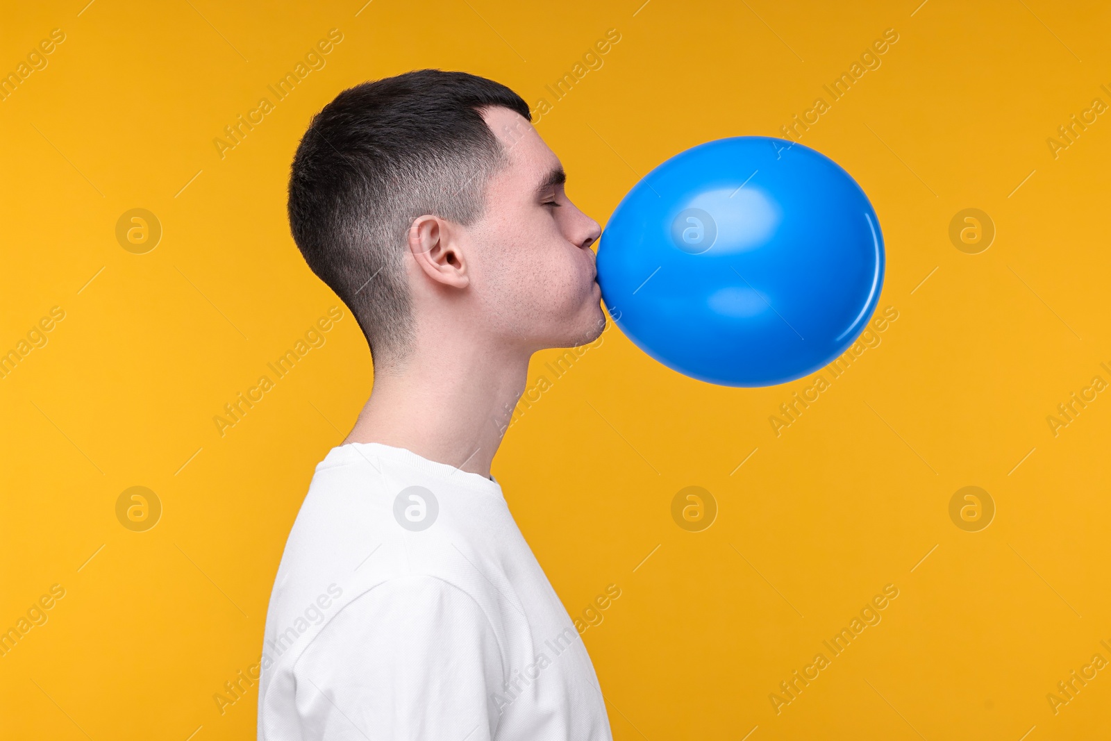 Photo of Young man inflating light blue balloon on yellow background