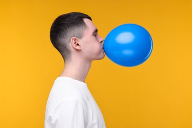 Young man inflating light blue balloon on yellow background