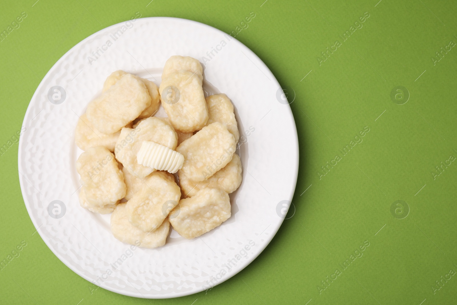 Photo of Plate of tasty lazy dumplings with butter on light green background, top view. Space for text