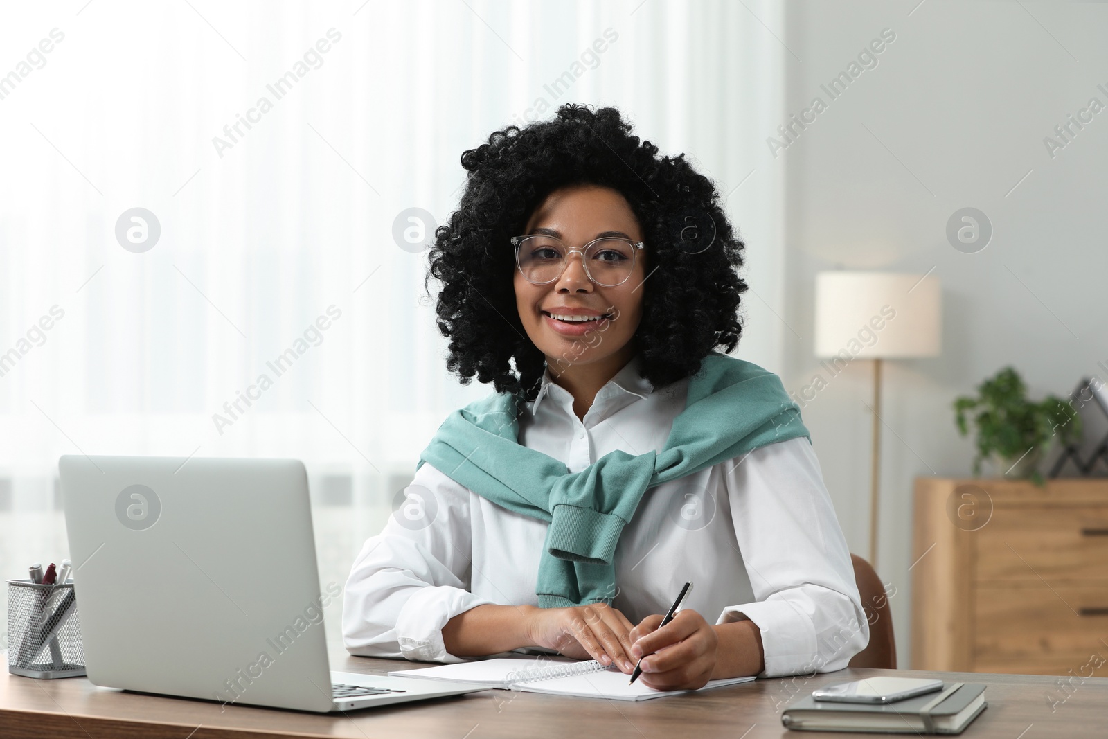 Photo of Happy young woman using laptop at wooden desk indoors