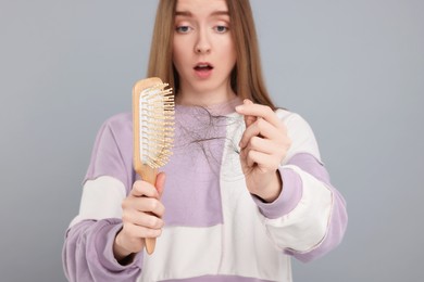 Woman untangling her lost hair from brush on light grey background, selective focus. Alopecia problem