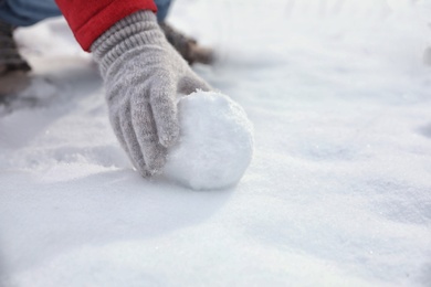 Photo of Young woman rolling snowball outdoors on winter day, closeup