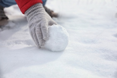 Young woman rolling snowball outdoors on winter day, closeup