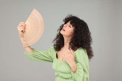 Photo of Woman with hand fan suffering from heat on light grey background