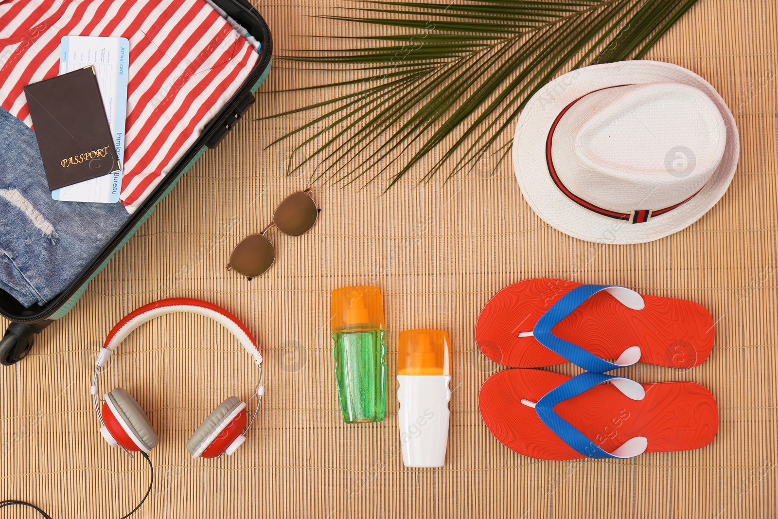 Photo of Flat lay composition with open suitcase and beach items on bamboo mat