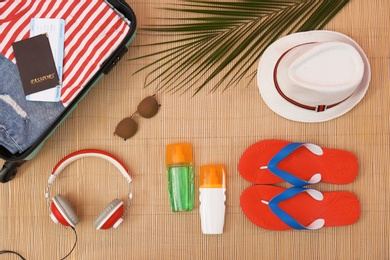 Flat lay composition with open suitcase and beach items on bamboo mat