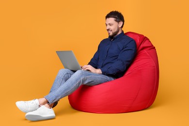 Photo of Happy man with laptop sitting in beanbag chair against yellow background