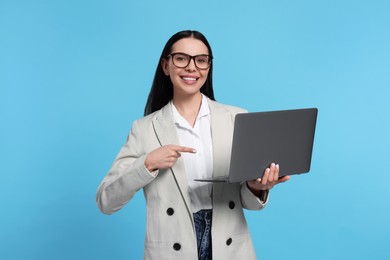 Photo of Happy woman pointing at laptop on light blue background