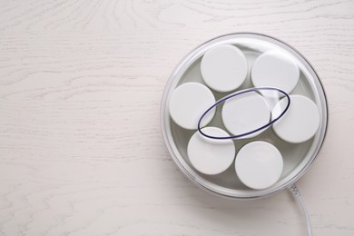 Modern yogurt maker with jars on white wooden table, top view. Space for text