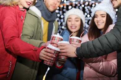 Happy friends with cups of mulled wine at winter fair