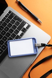 Photo of Blank badge, pen and laptop on orange background, top view