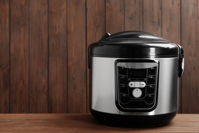 Photo of Modern powerful multi cooker on table against wooden background. Space for text