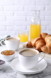 Photo of Tasty breakfast. Cups of coffee, fresh croissants and jam on white marble table