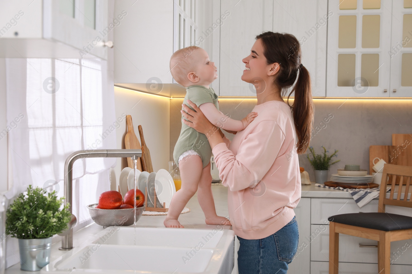 Photo of Happy young woman and her cute little baby spending time together in kitchen