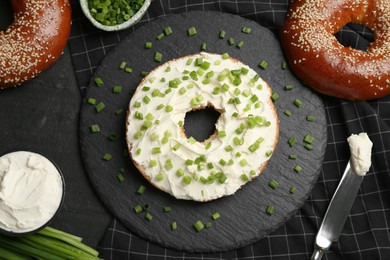 Photo of Delicious bagel with cream cheese and green onion on black table, flat lay