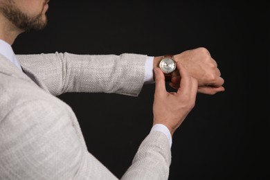 Photo of Businessman looking at wristwatch on black background, closeup. Time management