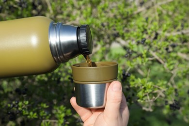 Photo of Man pouring hot drink into mug outdoors, closeup