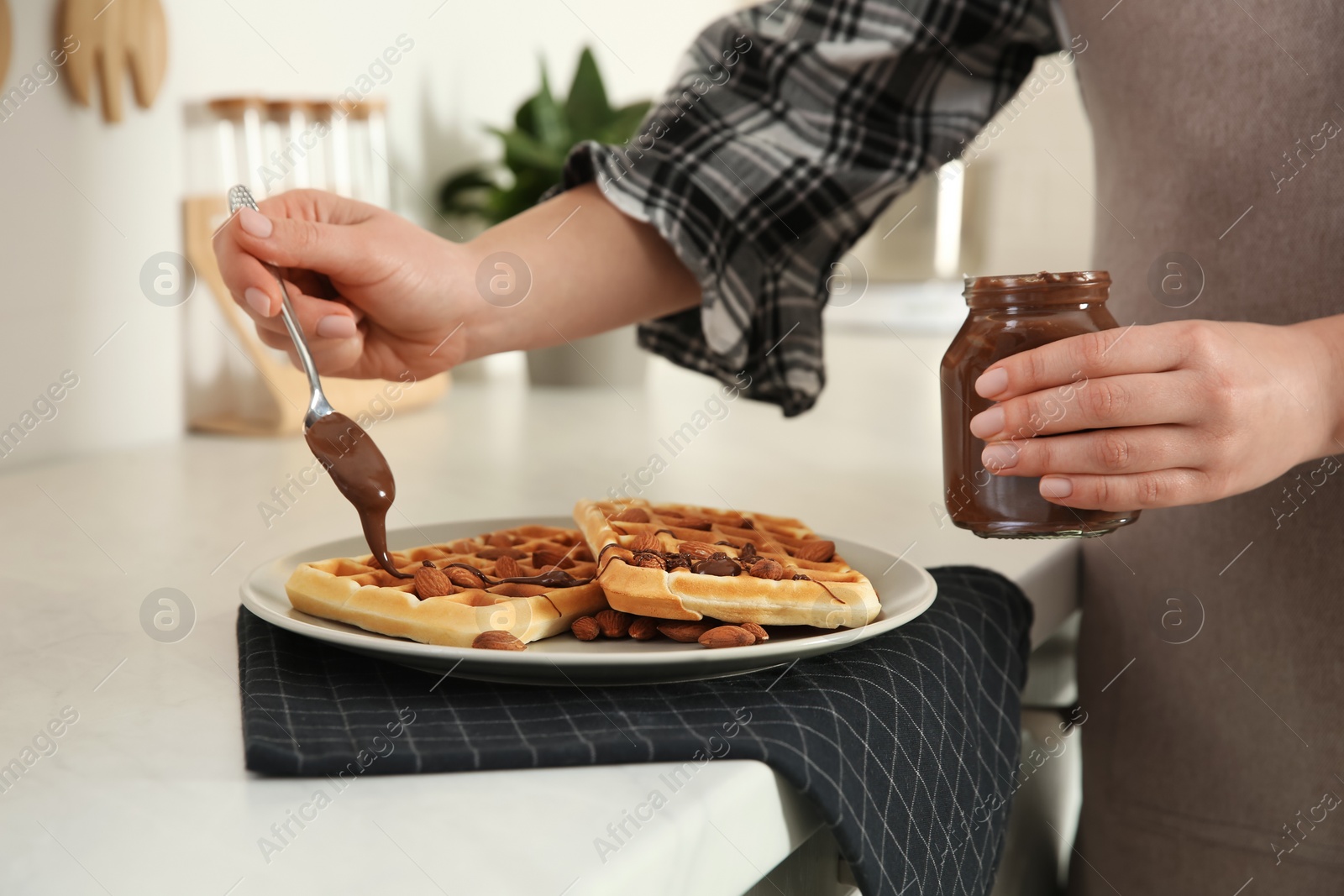 Photo of Woman decorating delicious Belgian waffles with chocolate cream at white countertop in kitchen, closeup