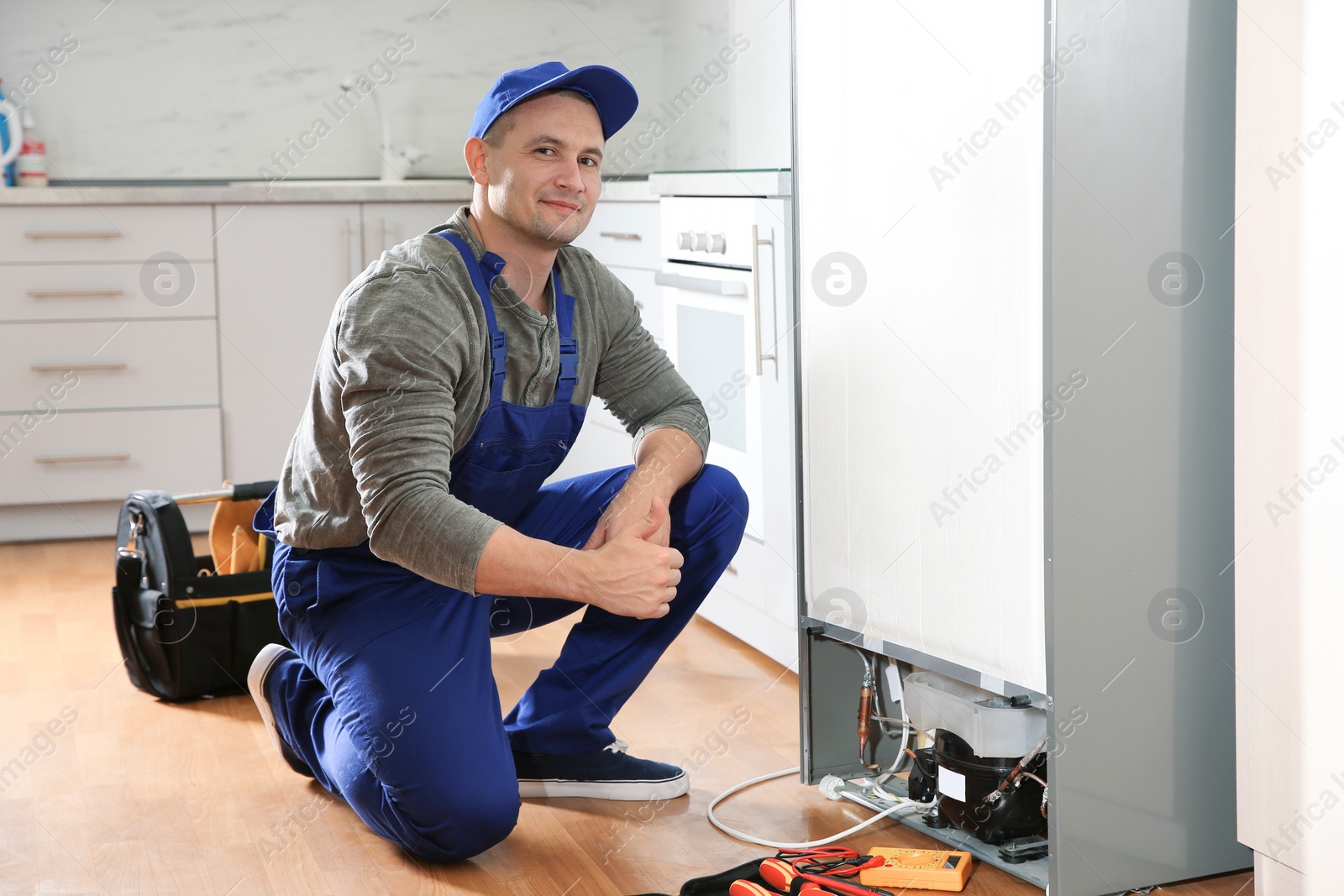 Photo of Male technician with tools near broken refrigerator indoors